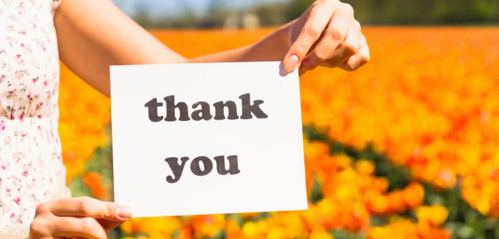 A woman holding a 'thank you' card in a field of tulips.