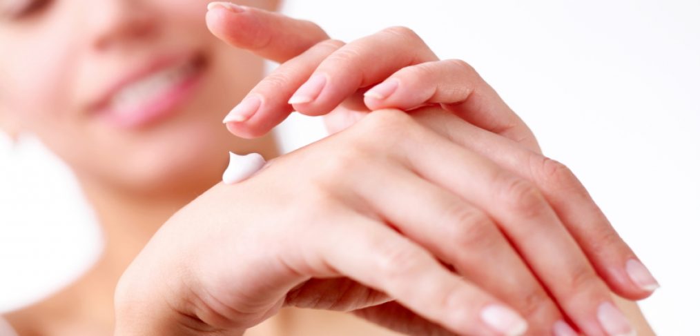 Smiling young woman applies cream on her hands.