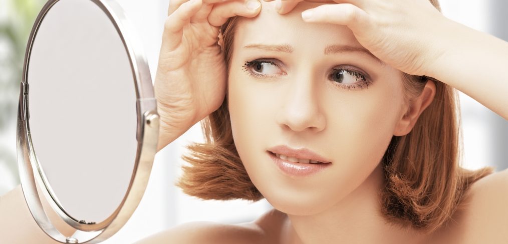 Young woman popping pimple in mirror