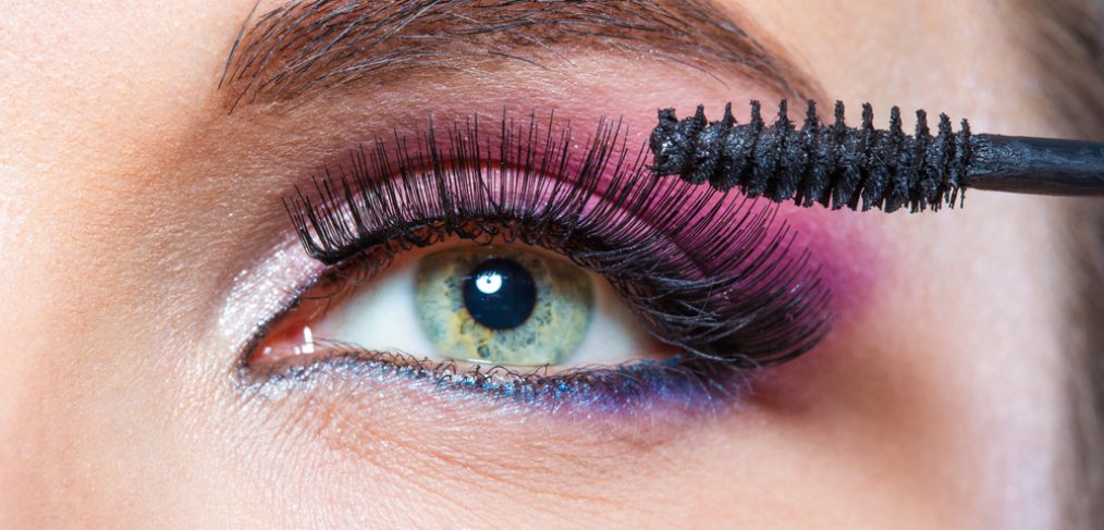 Woman with bright makeup applying mascara.