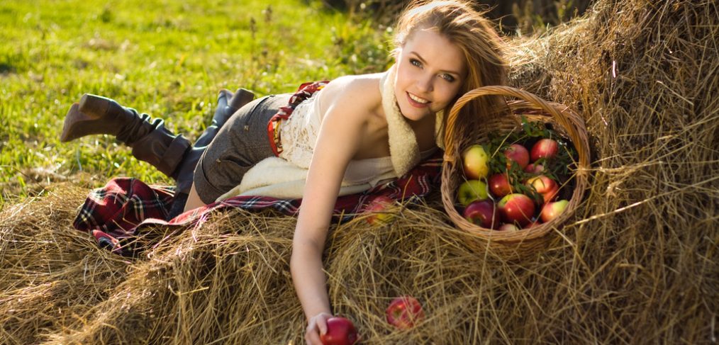 Woman with an apple in hand lying on hay.