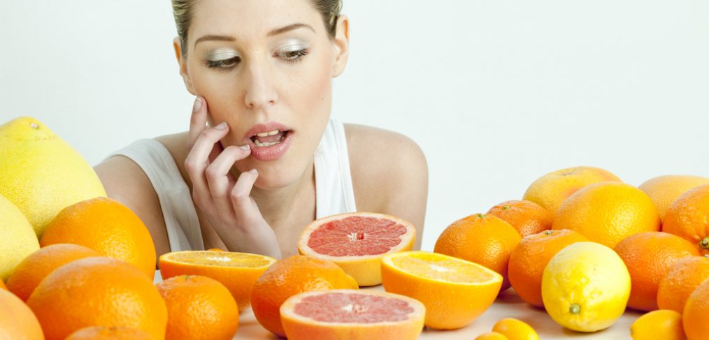 Woman surrounded by citrus fruits deciding what to eat.