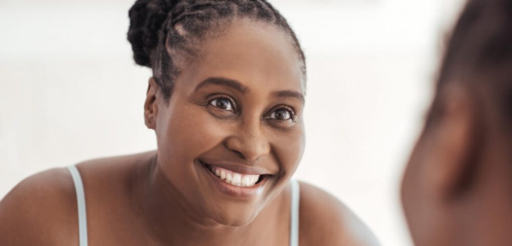 Happy smiling woman looking at herself in bathroom mirror