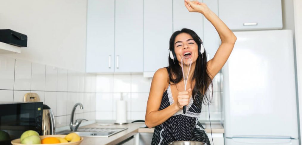 Happy young woman singing to herself in the kitchen, with headphones