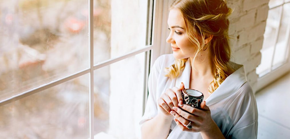 Young woman drinking tea next to window