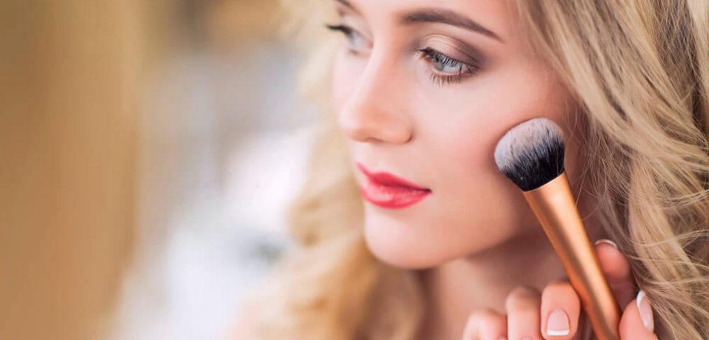 Makeup artist applying blush on beautiful woman's cheek