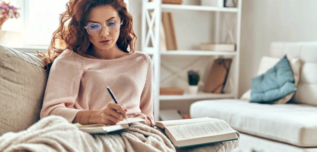 Focused woman writing in journal, on sofa at home